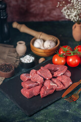 Close up view of fresh raw chopped meats and cutlery set on wooden board vegetables kitchen hammer on dark background