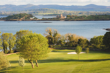 Scenic view of coastal golf hole and green and the Firth of Forth with the historic Inchcolm Abbey...