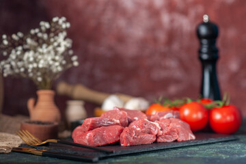 Front close view of fresh raw chopped meats and fork tomatoes on wooden board garlics on blurred background