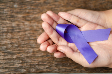 Purple ribbon for the awareness about the unacceptability of the violence against women on dark gray rustic wooden surface. Top view with space for text. Domestic violence awareness.