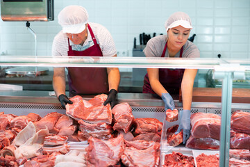 In local butcher shop, elderly male seller prepares order of pork ribs for regular customer. Seller assistant puts beef offal in window