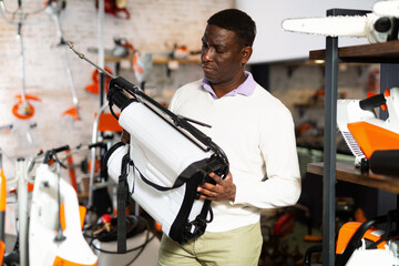 African-american man choosing shoulder sprayer in gardening tools store.