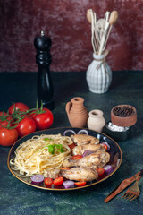 Front close view of raw pastas chickens and vegetables on a plate and cutlery set tomatoes spices wooden hammer cutlery set on green black mix colors background