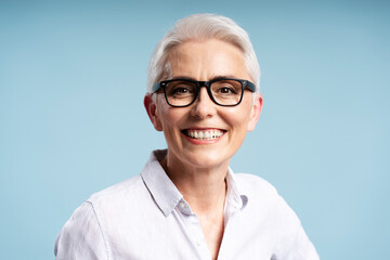 Portrait of smiling gray haired senior woman wearing stylish eyeglasses isolated on blue...