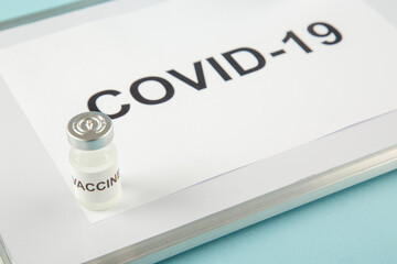 Front view of a sheet with COVID- and medicine ampoule on white desk on blue background