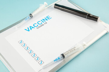 Front view of a sheet with COVID- vaccine ticks disposable syringe on white desk on blue background