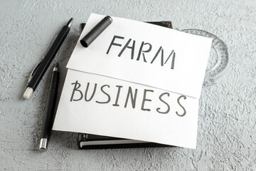 Front view of BUSINESS and FARM writings on white sheets ruler pens on gray sand background with free space