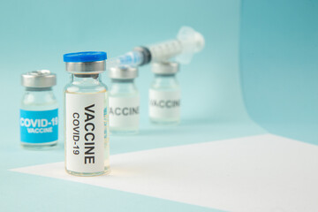 Front view of COVID- vaccine in medical ampoules and disposable syringe on the right side on pastel blue and white background