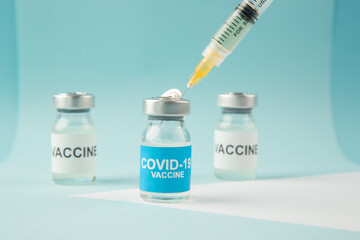 Front view of hand vaccine ampoules and syringe on pastel blue and white background with free space