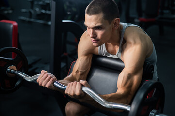Man doing EZ barbell bicep exercises on Scott bench. 