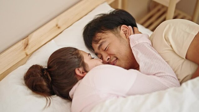 Man and woman couple lying on bed hugging each other kissing at bedroom