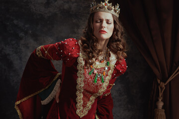 tired medieval queen in red dress with crown having backache