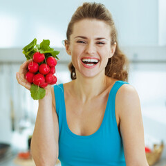 Smiling young woman holding bunch of radishes in kitchen