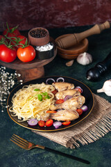 Front view of pasta meal with chickens and vegetables on a plate flowers on nude towel and fork foods spices on cutting board wooden hammer