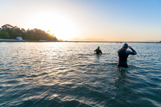 Wearing wetsuits, two men wade into the Aquatic Park Lagoon for an evening swim in the San Francisco Bay, California