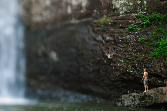 A man in a bathing suit stands next to a large waterfall in Tennessee, tilt-shift effect