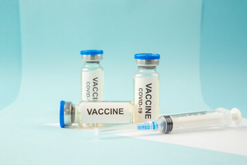 Horizontal view of COVID- VACCINE in closed ampoules and disposable syringe on pastel blue and white background with free space