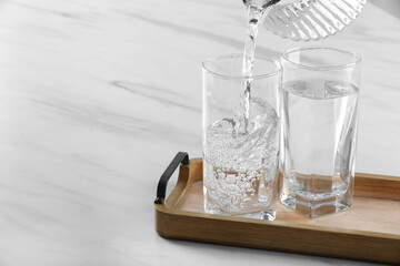 Pouring water from jug into glass at white marble table. Space for text