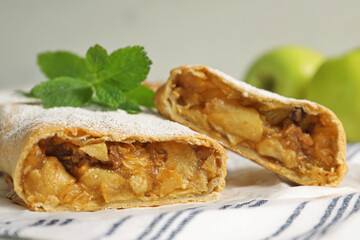 Delicious strudel with apples, nuts and powdered sugar on table, closeup