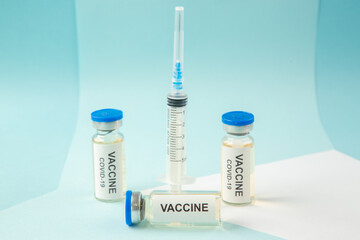 Horizontal view of vaccine in medical ampoules and empty disposable syringe on a white blank on blue background
