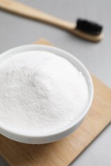 Bamboo toothbrush and bowl of baking soda on grey table, closeup
