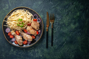Horizontal view of raw pastas chickens and vegetables on a plate and cutlery set on the right side on green black mix colors background