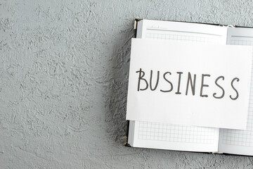 Overhead view of BUSINESS writing on white sheet on new open notebook on the left side on gray sand background