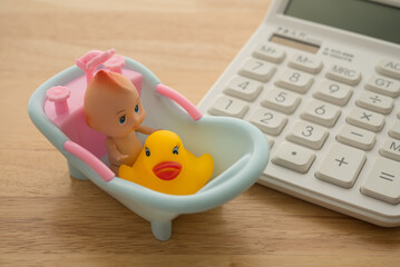Cute baby figure toy and calculator on wooden background copy space. Concept of cost of parenting, financial money management and planning, education investment, family expense, stress feeling.