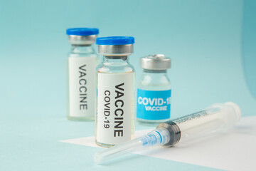 Side view of COVID- vaccine ampoules and disposable syringe on pastel blue and white background