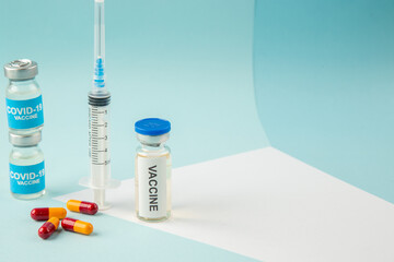 Side view of empty disposable syringe and capsules on a white blank covid- vaccines on the right side on blue background