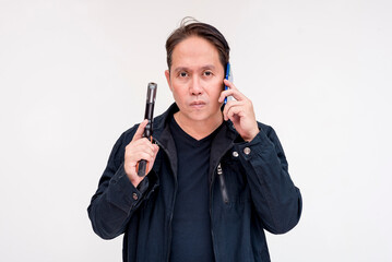 A police negotiator looking at the camera listens to the demands of a kidnapper via phone while brandishing a gun. Isolated on a white backdrop.