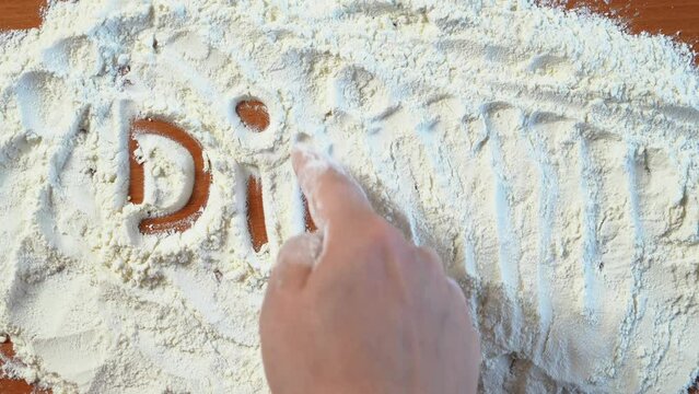  Hand writes word dinner finger on scattered white flour. Advertising screensaver for cooking show, master class with cooking, baking recipes. Recipes for culinary pastries. Coffee and pastry menu.