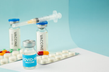 Side view of vaccine in medical ampoules packed pills capsules and disposable syringe on the right side on white blue mix colors background