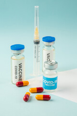 Side view of vaccines for treatment Covid- in medical ampoules capsules and syringe on white blue background