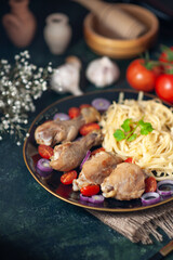 Side view of pasta meal with chickens and vegetables on a plate flowers spices on nude towel wooden hammer