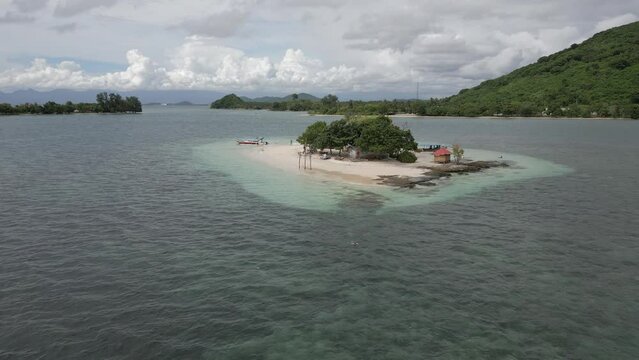 Aerial retreats from sml tropical islet as man swims in clear water