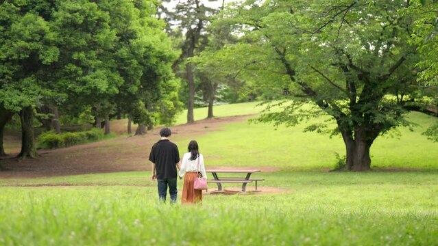 新緑の公園を散歩するカップルの後ろ姿のワイドショット
