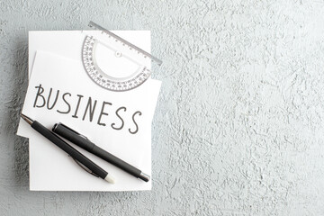 Top view of BUSINESS writing on white sheet ruler pens on the right side on gray sand background with free space