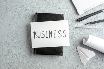 Top view of BUSINESS writing on white sheet on black notebook pens ruler paper plane desk blank on...