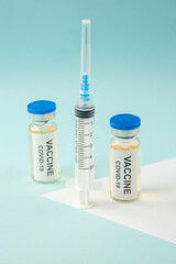 Top view of COVID- vaccine in medical ampoules and empty disposable syringe on white sheet on blue wave background