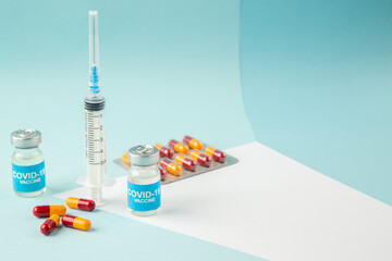 Top view of empty disposable syringe and capsules on a white blank covid- vaccines on the right side on blue background