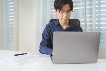 Happy Asian businessman, male businessperson using computer laptop with paperwork on desk at office. Professional entrepreneur business man wear eyeglasses, sitting to working, planning on workplace.