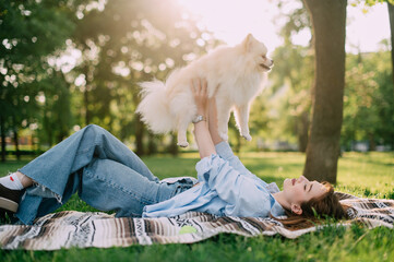 A young woman lies on the grass and holds her Pomeranian dog in her arms.