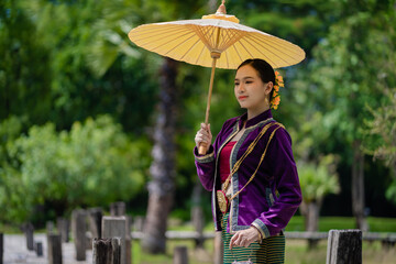 Beautiful pretty young Asian woman wearing a millionaire traditional Thai dress Lanna style standing with an antique silver bag and umbrella in a green natural park.