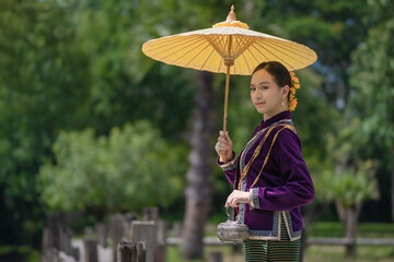 Beautiful pretty young Asian woman wearing a millionaire traditional Thai dress Lanna style standing with an antique silver bag and umbrella in a green natural park.