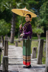 Beautiful pretty young Asian woman wearing a millionaire traditional Thai dress Lanna style standing with an antique silver bag and umbrella in a green natural park.