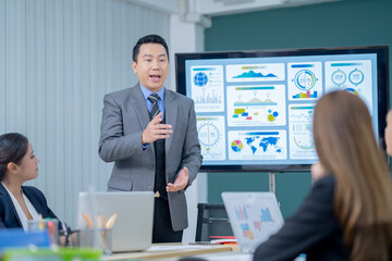 Office Conference Room Meeting Presentation: asian Businessman Talks, Uses Wall TV to Show Company Growth with Big Data Analysis, Graphs, Charts, Infographics. Multi-Ethnic e-Commerce Startup 