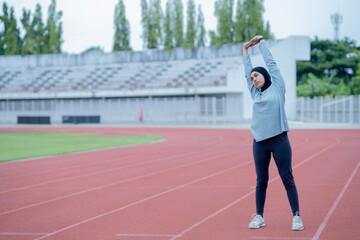 Obraz premium A young asian Muslim woman wearing a black hijab is exercising and running at an outdoor stadium in the morning. Modern Muslim woman concept, Muslim woman sport concept, Islam