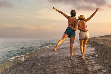 Sunset Beach Stroll: Joyful Friends Embracing Adventure - Two young friends, one wearing a straw...