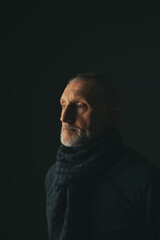portrait of a sad adult man with a white beard and a scarf on a black background, close-up, selective focus